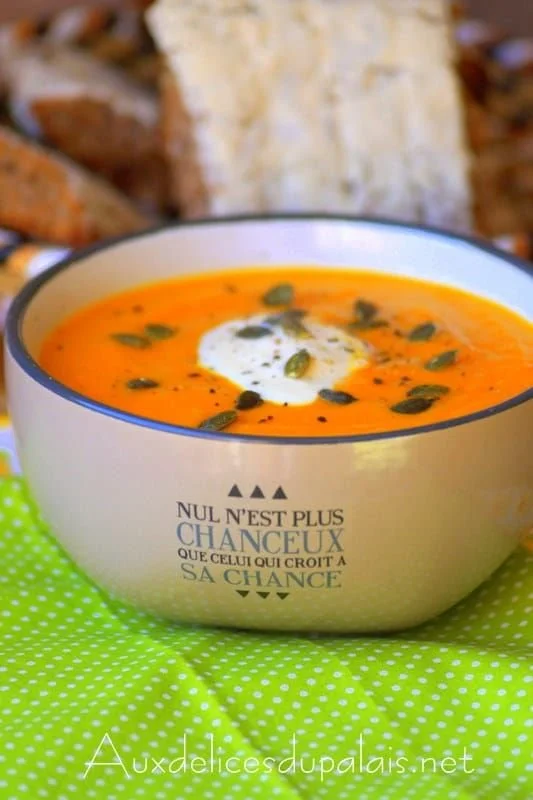 Soupe de potiron aux carottes servie dans un bol, garnie de graines et de crème.